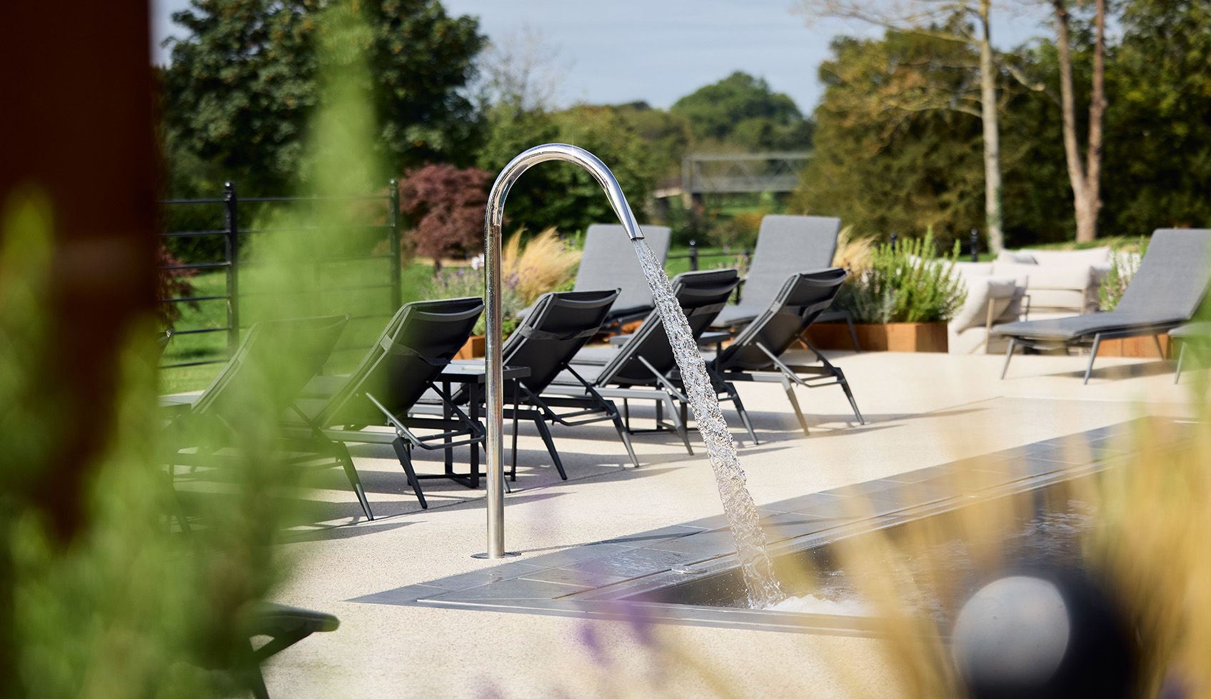 Outdoor spa area with loungers and a water feature surrounded by greenery